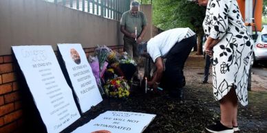 People gather by memorial plaques and flowers at a remembrance site.