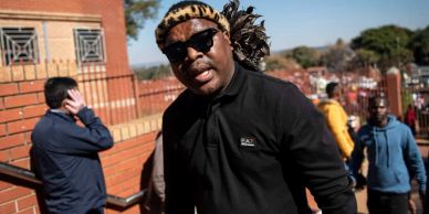 Man wearing sunglasses and a leopard print hat outdoors.