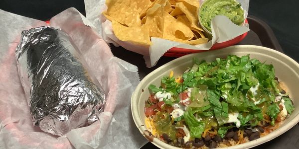 A foil-wrapped burrito, chips with guacamole, and a loaded burrito bowl.