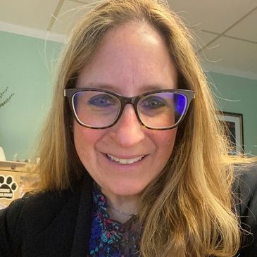 Smiling woman with glasses and long blonde hair indoors.