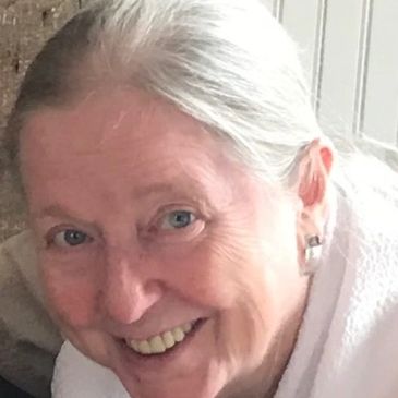 Smiling elderly woman with white hair and blue eyes indoors.