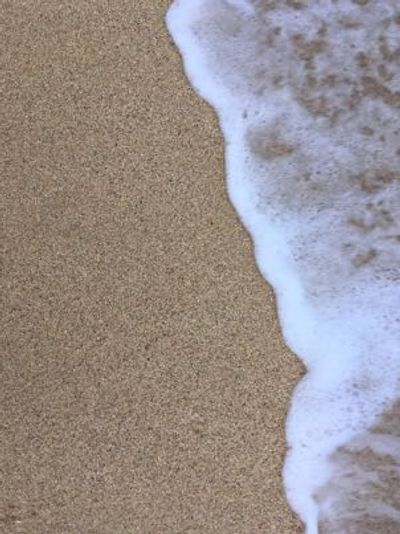 A closeup photograph of a small ocean wave lapping up on a sandy beach.
