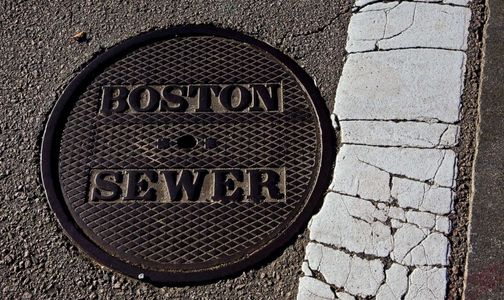 Manhole cover labeled Boston Sewer on cracked pavement.