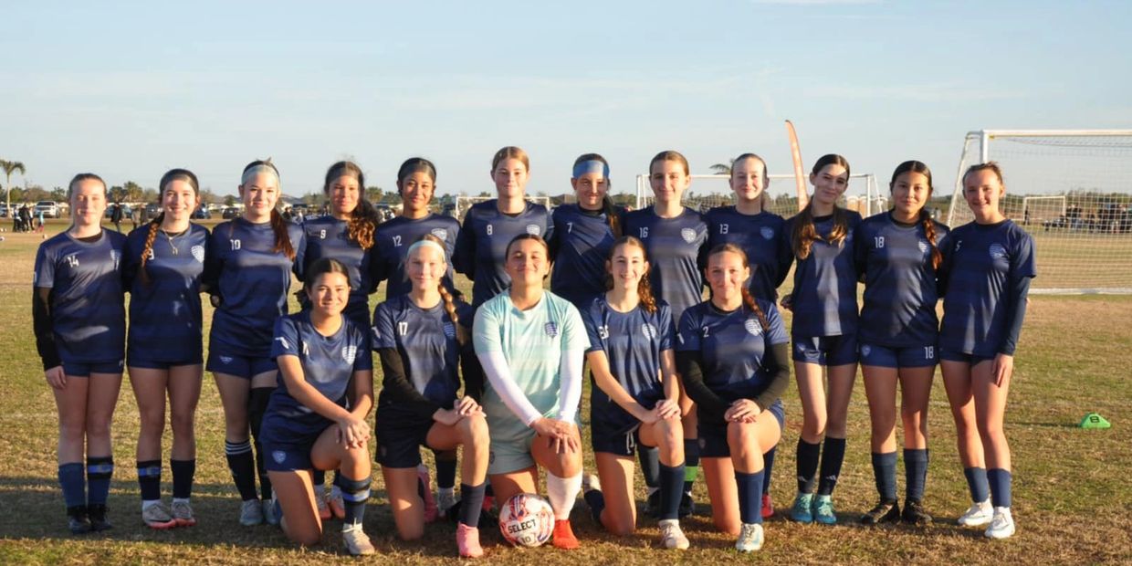 Youth girls' soccer team posing for a group photo on a field.