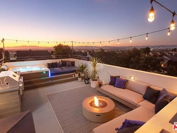 Cozy rooftop patio with fire pit, string lights, and hot tub at sunset.