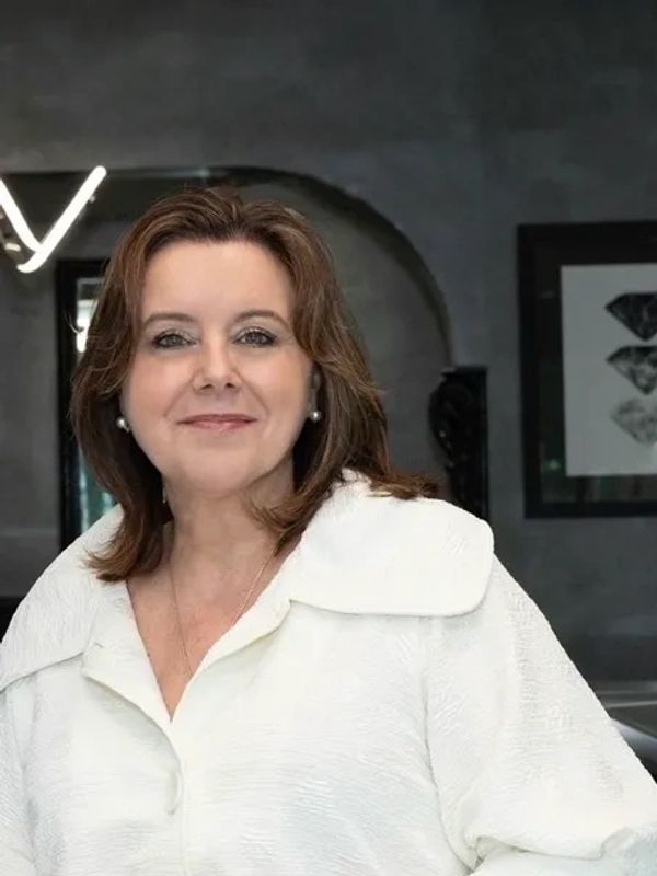 Smiling woman with brown hair wearing a white textured jacket indoors.
