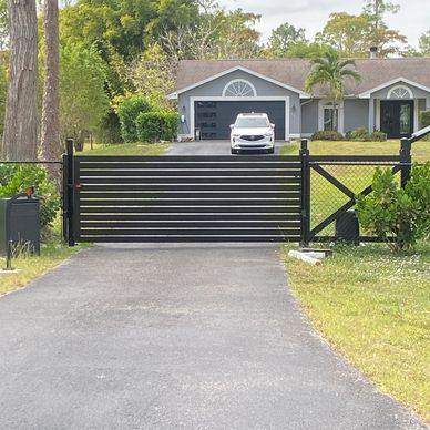 Driveway gate with a white car and house in the background.
