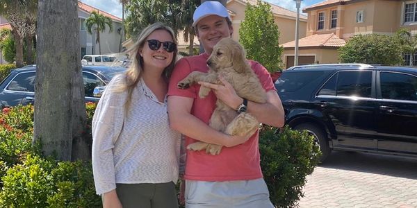 Happy couple outdoors holding a golden retriever puppy on a sunny day.