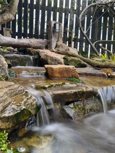 A small, serene backyard waterfall flowing over rocks and moss.