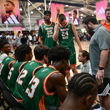 Basketball team huddling during a timeout at a busy indoor court.
