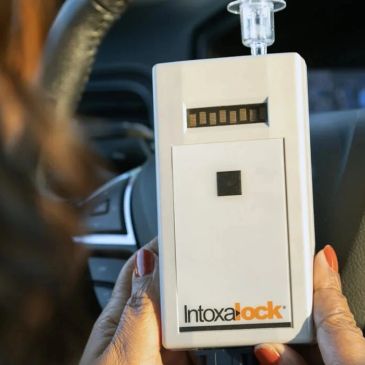 Person holding an Intoxalock breathalyzer device in a car.