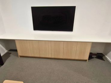 Wall-mounted TV above a wooden cabinet on a carpeted floor.