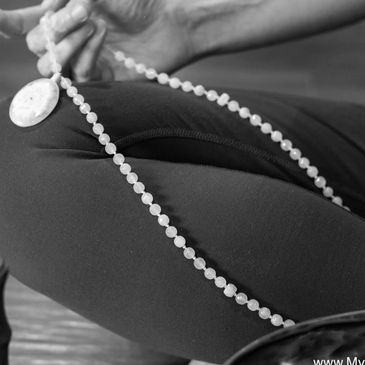 Person holding a rosary while seated, dressed in dark pants.