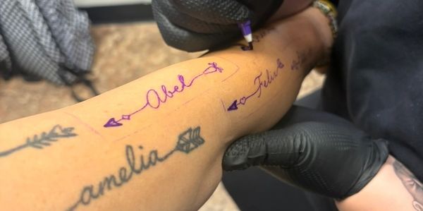 Person writing tattoo names on forearm with purple marker.