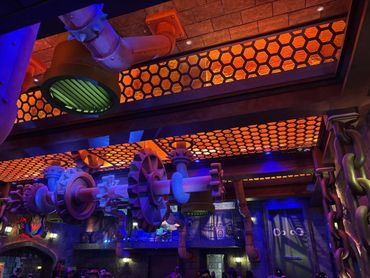 Futuristic industrial ceiling with glowing orange hexagonal lights and mechanical gears.