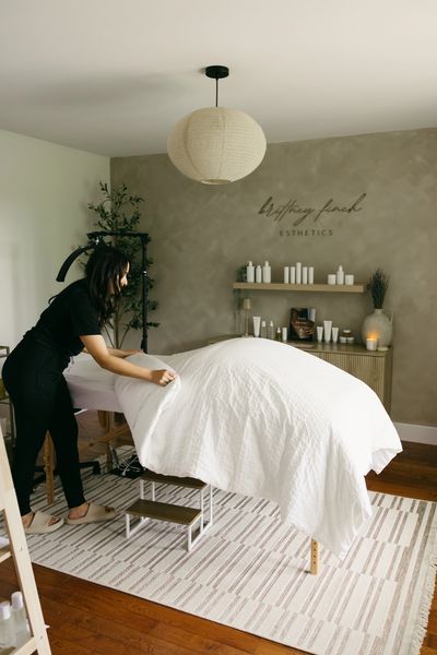 A woman prepares a spa bed in a serene aesthetics room.