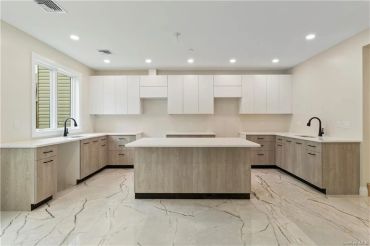Modern kitchen with light wood cabinets and marble flooring.