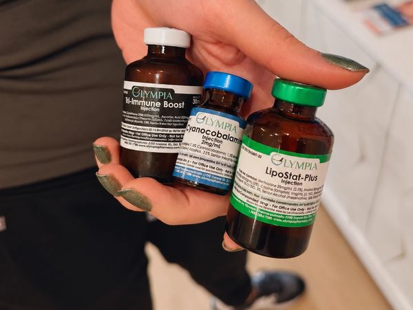 Hand holding three medicine bottles labeled Olympia injections.
