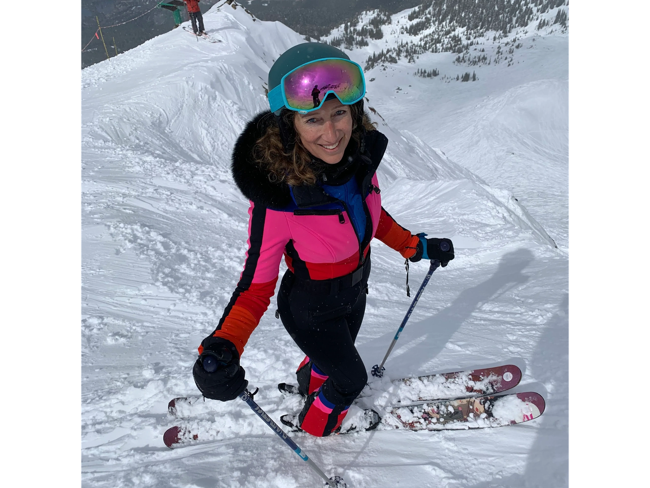 Smiling skier in colorful outfit on snowy mountain.
