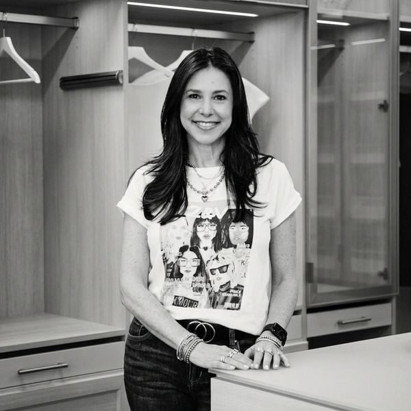 Smiling woman standing in a modern closet space wearing a graphic tee and accessories.
