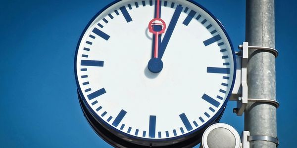 Large outdoor clock showing 12:03 against a blue sky.