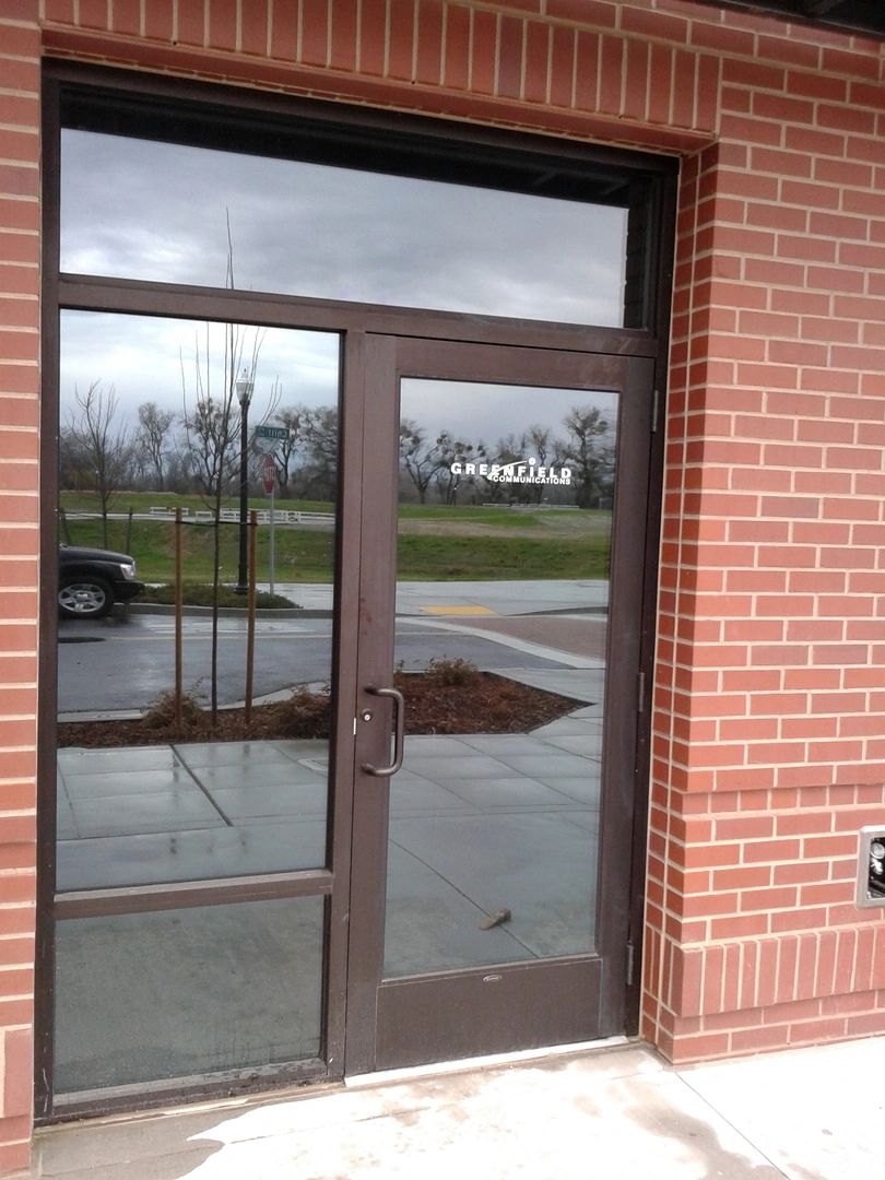 Glass door entrance with "Greenfield Communications" sign.