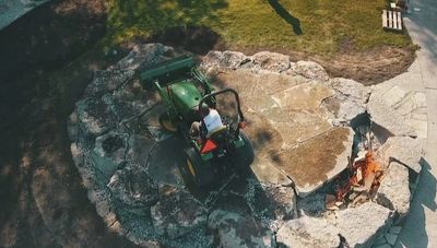 Ty, riding a tractor, finishing a huge beachside patio / firepit build off with its inaugural fire.