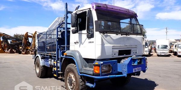 White and blue heavy-duty truck parked on an industrial lot under a clear sky.
