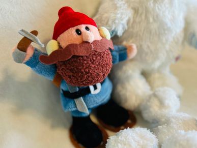 Plush toy dwarf with red hat and brown beard holding an axe.