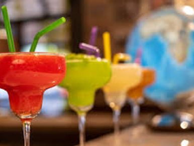 Colorful cocktails with straws lined up on a bar counter.