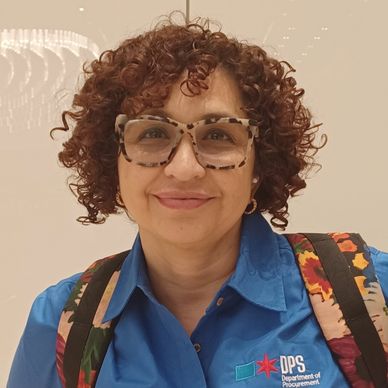Smiling woman with curly hair wearing large glasses and a blue DPS shirt.