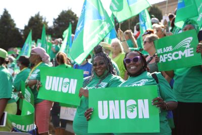 Smiling people holding green union signs at a rally.
