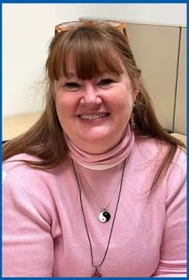 Smiling woman in pink sweater with yin-yang necklace.