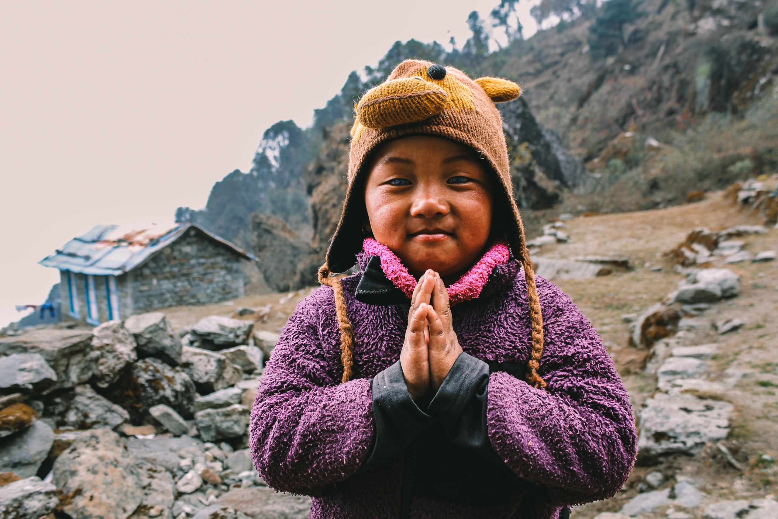 Child in a cute animal hat with hands pressed together in a greeting.