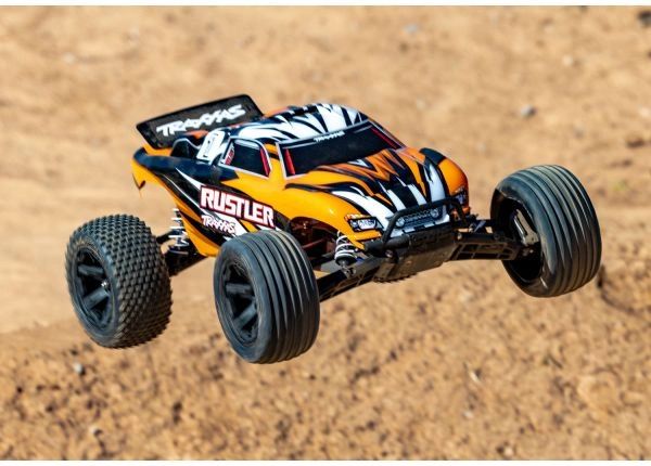 Orange and black RC car mid-air on dirt.