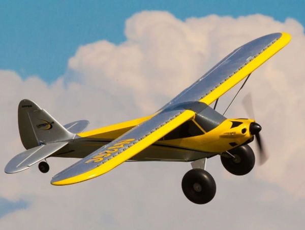 Yellow model airplane flying against cloudy sky.