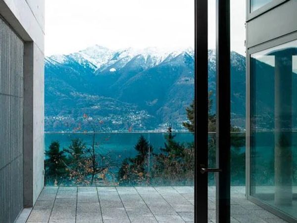 Modern balcony with glass railing overlooking snowy mountains and a lake.
