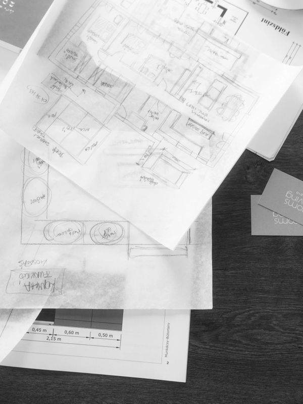 Black and white photo of architectural floor plans and design sketches on a wooden table.