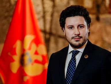 Man in suit with a red and yellow flag in the background.
