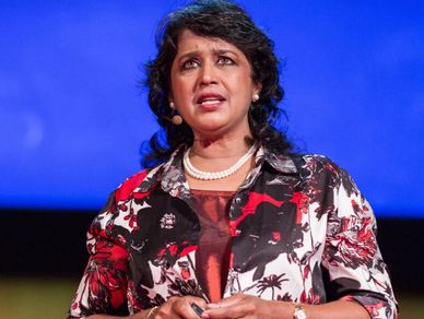 Woman speaking on stage with a blue background.