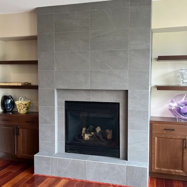 Modern gray tiled fireplace with wooden shelves and cabinets.
