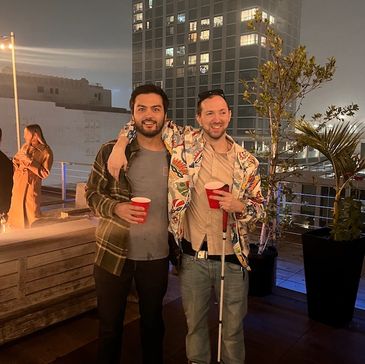 Two friends enjoying a rooftop party at night with drinks in hand.