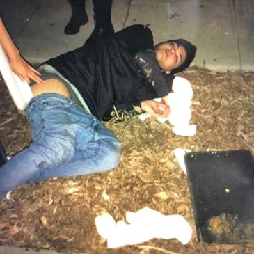 A man lies on the ground while another person touches his lower back.