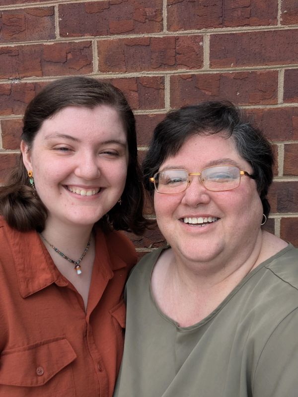 Two women smiling in front of a brick wall.