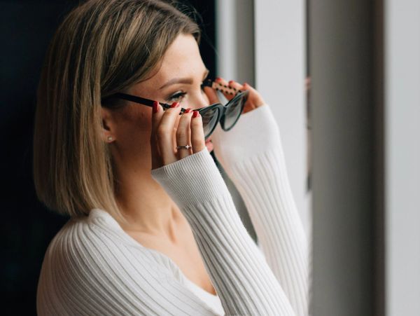 Woman adjusting sunglasses while looking out a window.