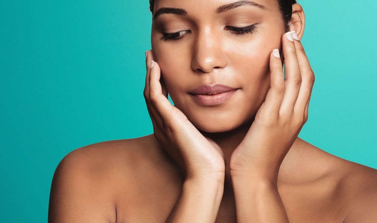 Darker-skinned woman with her hands near her face, and eyes glancing down.