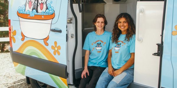 Two women in blue shirts sitting by a colorful van.