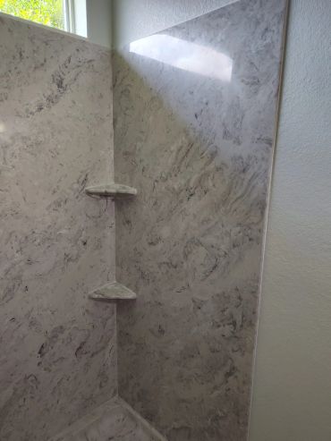 Marble-patterned shower corner with two small corner shelves and natural light.