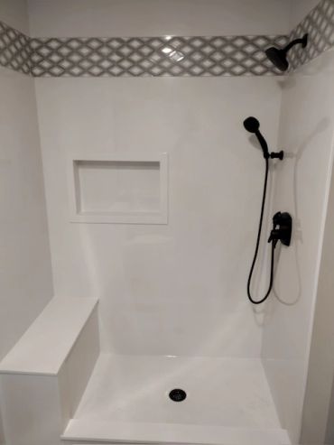 A modern white shower with black fixtures and a bench.