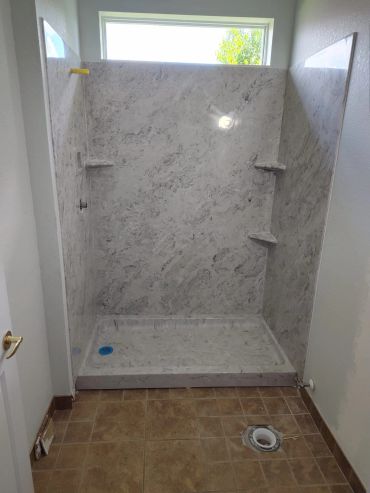 Newly installed marble shower stall with built-in shelves and window above.